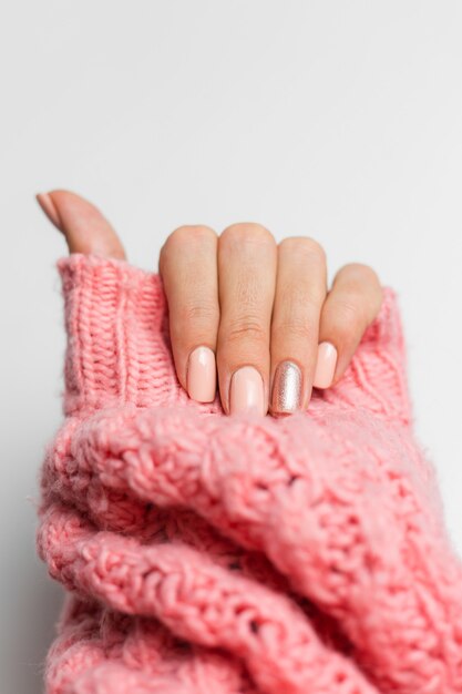 Pretty nude color manicure, one finger shiny golden, on knitted pink wool pillover background