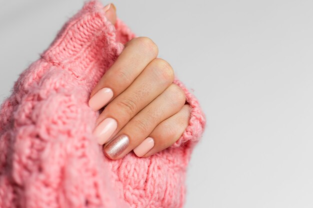 Pretty nude color manicure, one finger shiny golden, on knitted pink wool pillover background