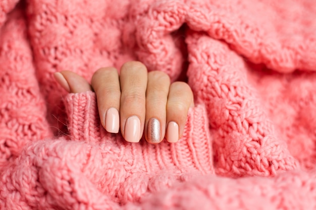 Pretty nude color manicure, one finger shiny golden, on knitted pink wool pillover background