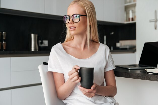 Pretty pensive lady with cup of tea sitting in the kitchen