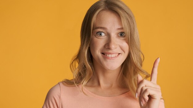 Pretty positive blond girl keep finger up having idea isolated on yellow background. New idea gesture