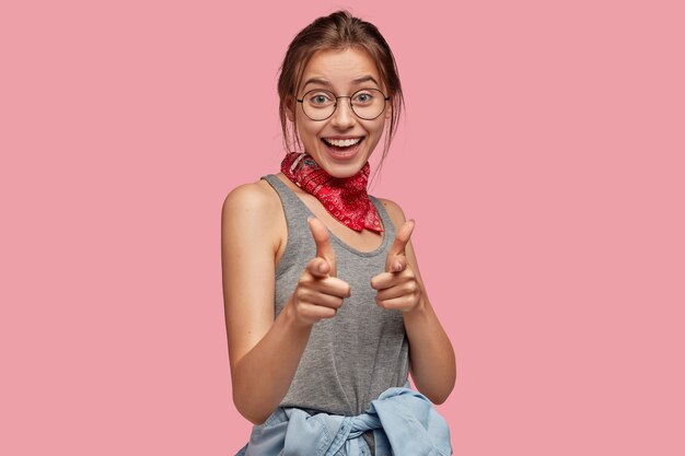 Pretty positive European girl in round spectacles, red bandana, grey t shirt