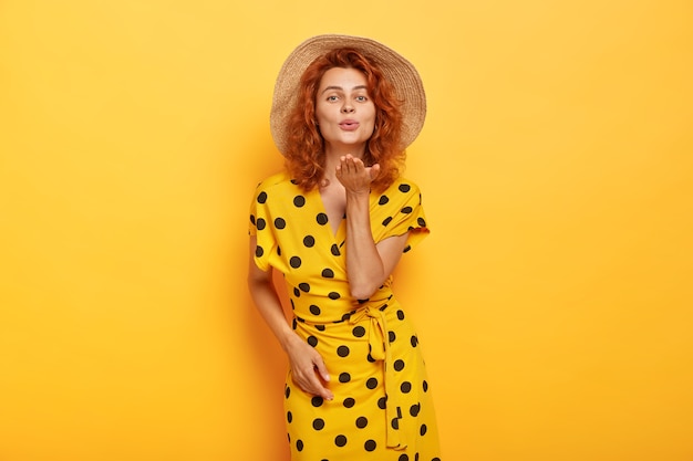 Free photo pretty redhead woman posing in yellow polka dress and straw hat