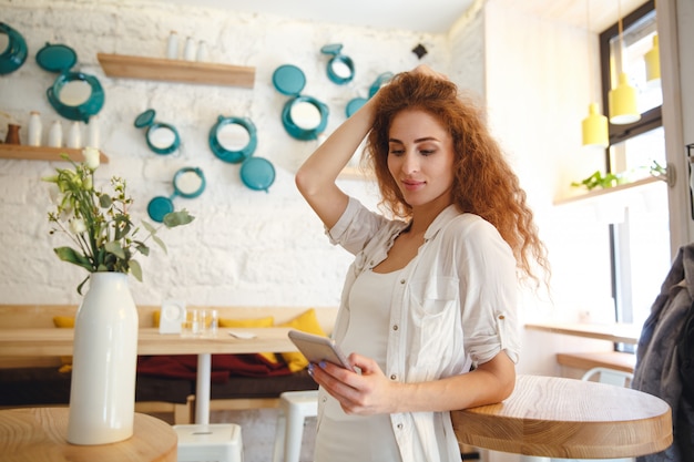 チャットしながらカフェに立っているかなり赤毛の若い女性