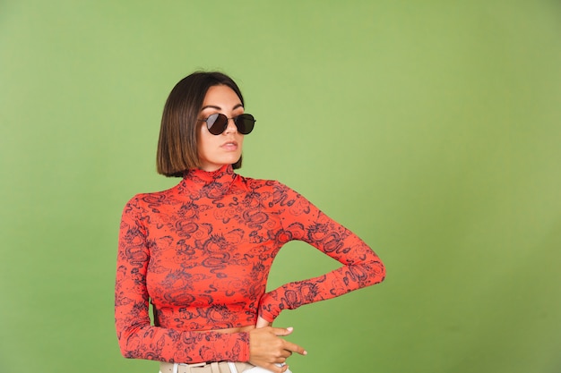 Pretty short hair woman with golden earrings, sunglasses, red china dragon printed blouse on green