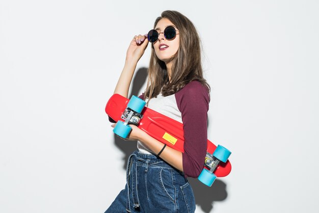 Pretty skater girl in casual clothes and sunglasses holding red skateboard