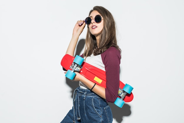 赤いスケートボードを保持しているカジュアルな服とサングラスのかわいいスケーターの女の子