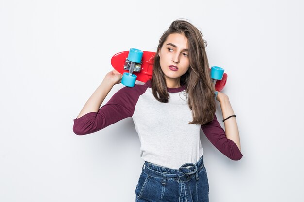 Pretty skater girl holding red skateboard on her back isolated on white wall