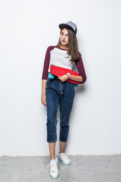 Pretty skater girl holding red skateboard in her hands isolated on white wall