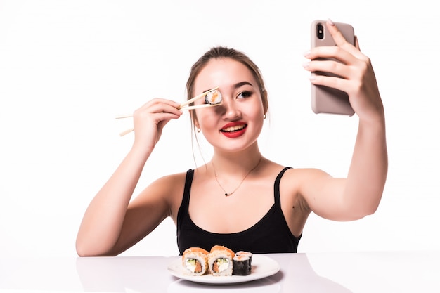 かなり笑顔のアジアの女性は巻き寿司で彼女の目を覆い、彼女の電話でselfieを作る