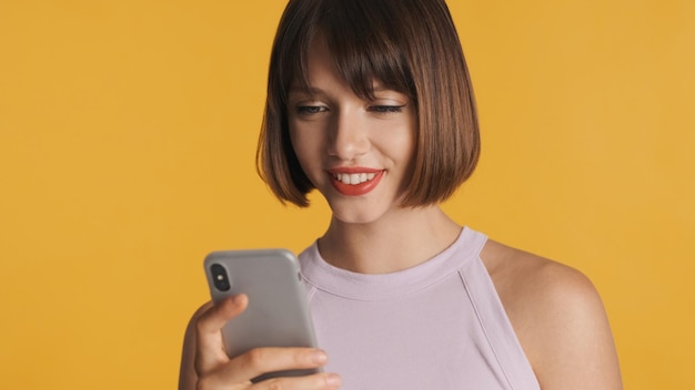 Pretty smiling brunette girl chatting with friends online on smartphone isolated on colorful background