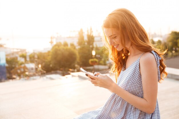 スマートフォンを使用してドレスでかなり笑顔の生姜女