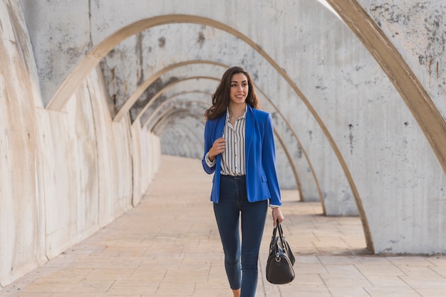 Pretty smiling girl holding her handbag and walking