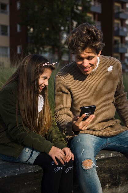 Довольно улыбается девушка, сидя в парке с ее отец, проведение сотовый телефон