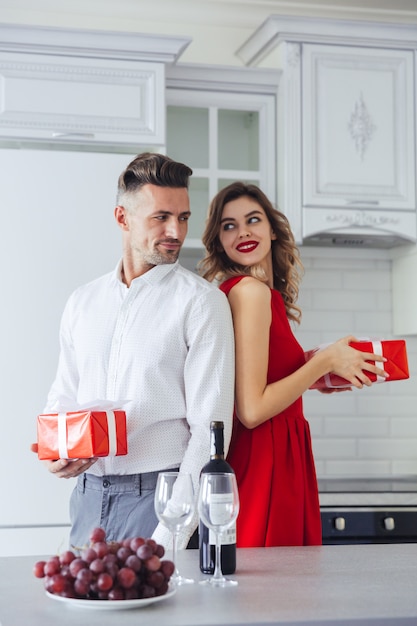 Pretty smiling lovers giving present to each other at home, valentines day concept