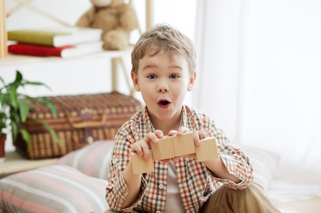 Pretty smiling surprised boy playing with wooden cubes at home