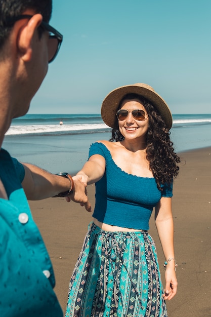 Pretty smiling woman pulling man to beach 