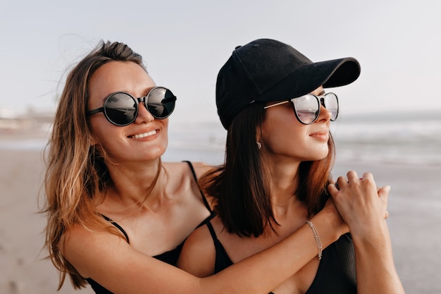 Pretty smiling young women walking on a beach Two best friends strolling along the ocean shore on a summer day enjoying vacation and looking dreamly on the ocean