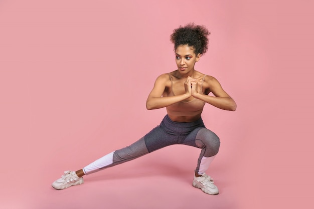 Free photo pretty sportive african female making exercises , posing on pink bagkground.