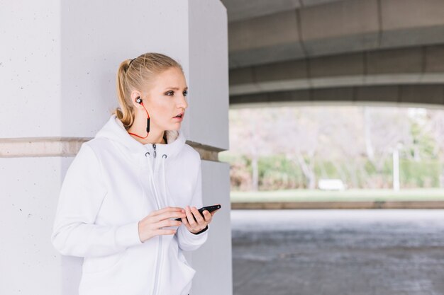 Pretty sportswoman browsing smartphone near column