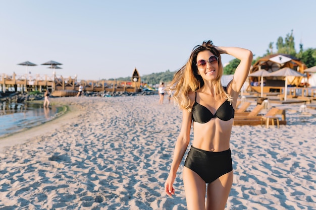 Красивая стильная женщина, одетая в черный купальный костюм на летнем пляже