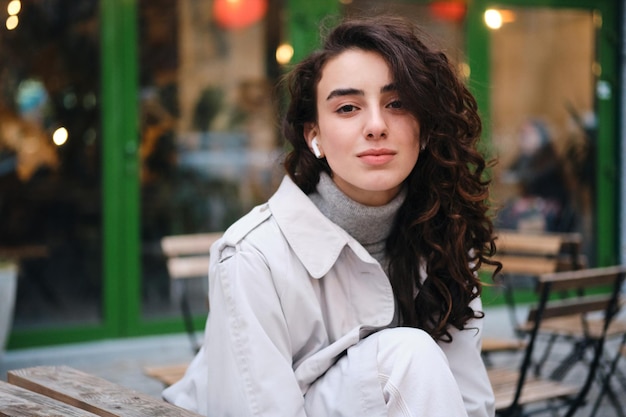 Pretty stylish brunette girl wistfully looking in camera while resting on city street