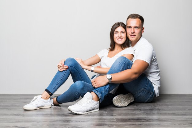 Pretty stylish couple hugging together while sitting on the floor isolated on white background