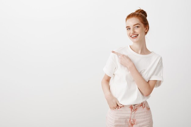 Pretty stylish redhead girl pointing finger left and smiling