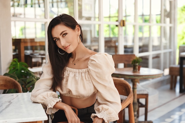 Pretty tanned woman sitting in hotel restaurant and smiling