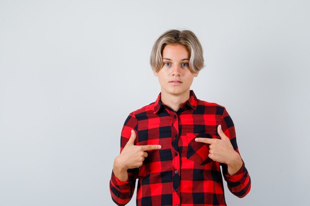 Pretty teen boy in checked shirt pointing at himself and looking puzzled , front view.