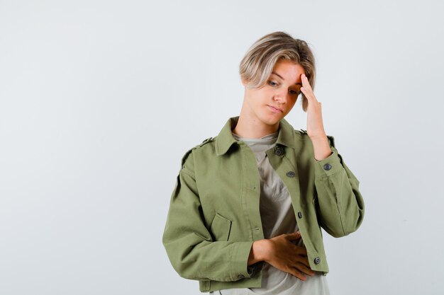 Pretty teen boy in green jacket leaning head on hand and looking sad , front view.