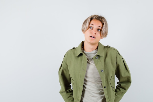 Pretty teen boy in green jacket looking upward and looking thoughtful , front view.