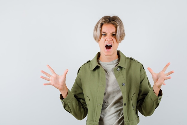 Pretty teen boy in green jacket showing claws imitating a cat while screaming and looking aggressive