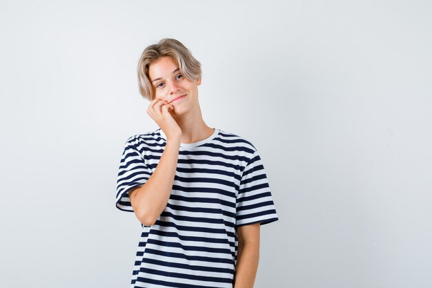 Pretty teen boy leaning cheek on hand in striped t-shirt and looking jolly , front view.