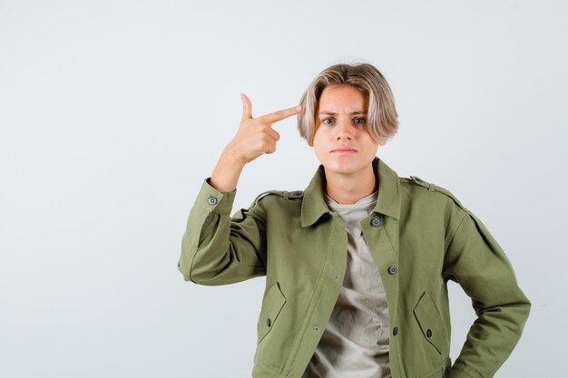 Pretty teen boy pointing at his head in green jacket and looking perplexed