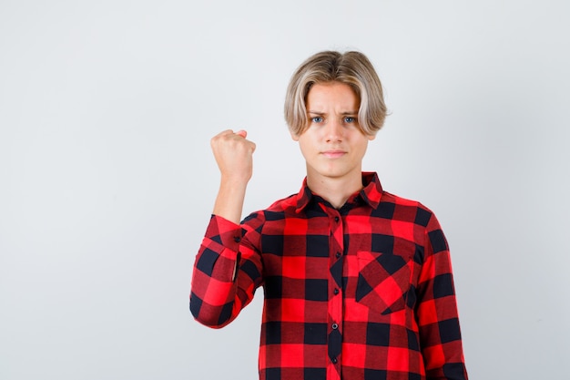 Foto gratuita ragazzo abbastanza teenager che mostra il pugno chiuso in camicia a quadri e sembra orgoglioso, vista frontale.