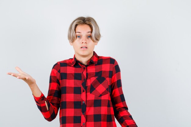 Pretty teen boy showing helpless gesture in checked shirt and looking clueless. front view.