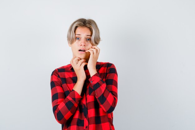 Pretty teen boy with hand on cheek in checked shirt and looking terrified , front view.