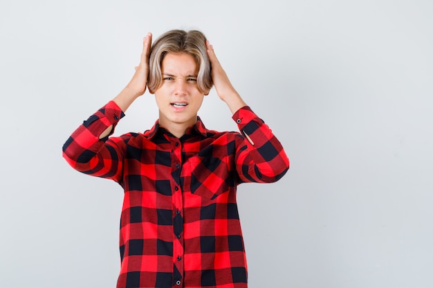 Pretty teen boy with hands on head in checked shirt and looking annoyed. front view.