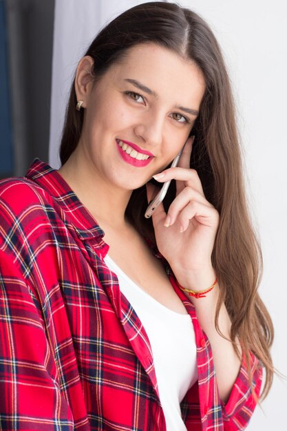 Pretty teenage girl making phone call Cute happy young woman smiling wide while talking at phone and looking straight into camera