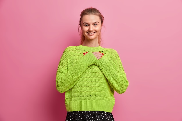 Foto gratuita bella ragazza adolescente con sorrisi di capelli pettinati esprime piacevolmente apprezzamento fa gesto di gratitudine