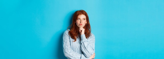 Free photo pretty teenage girl with red hair thinking looking upper left corner thoughtful pondering something