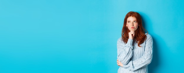 Free photo pretty teenage girl with red hair thinking looking upper left corner thoughtful pondering something