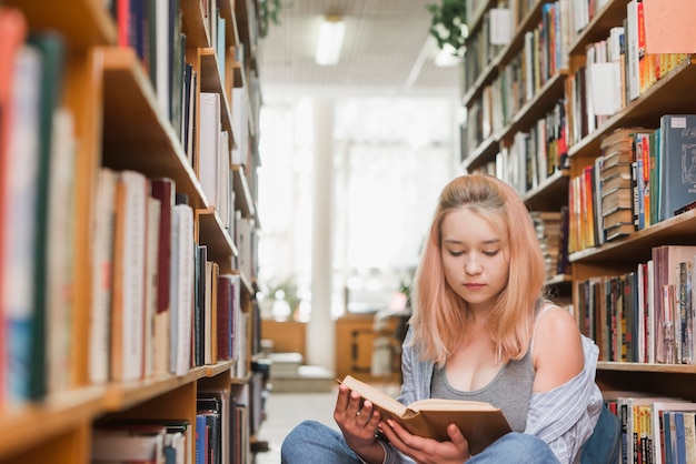 Pretty teenager reading near bookshelves