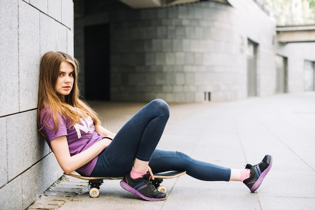 Pretty teenager on skateboard leaning on wall