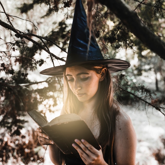 Довольно ведьма, читающая древнюю книгу заклинаний в солнечном лесу