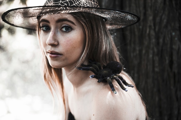 Free photo pretty witch with spooky spider in forest daytime