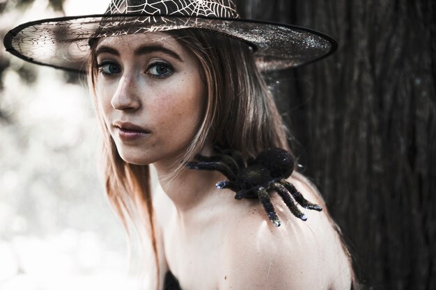 Pretty witch with spooky spider in forest daytime