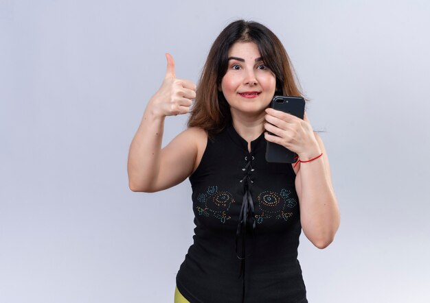 Pretty woman in black blouse looking happy thumbs up holding phone 