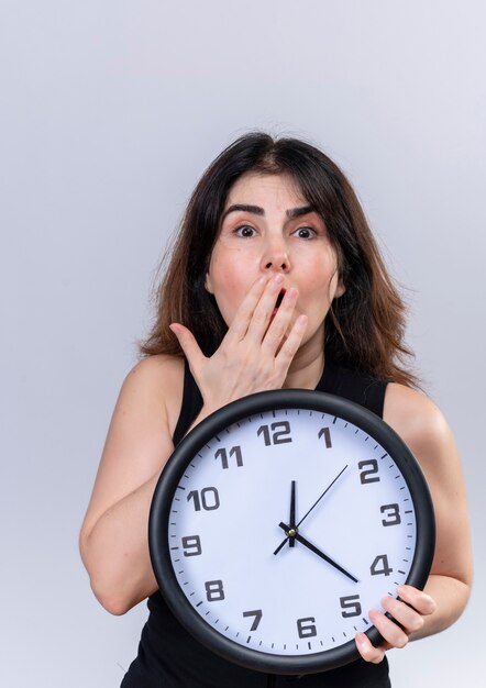 Pretty woman in black blouse looking scared for being late holding clock 